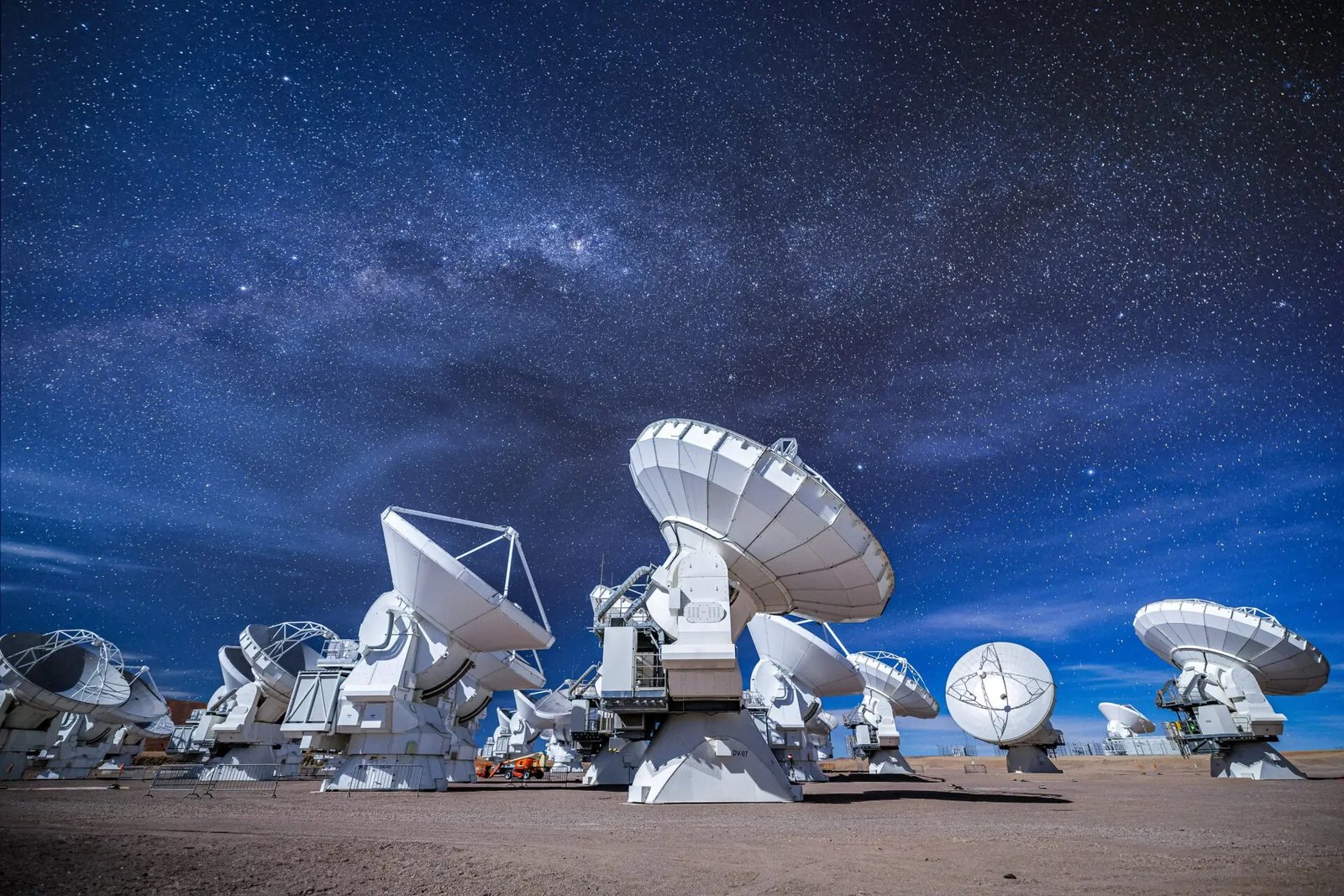 Vita radioantenner på en torr högplatå om natten, under en djupblå himmel full av stjärnor och med ett svagt band av Vintergatan.