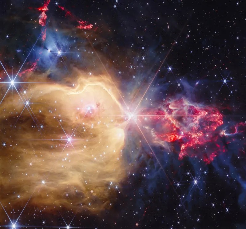 A bright star with eight long spikes sits at the centre; a golden cloud fills the left half, ragged red gas spreads to the right and a blue patch sits at the upper left, against a dark star field.